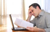 Man sitting at his desk with a laptop and bills  looking concerned